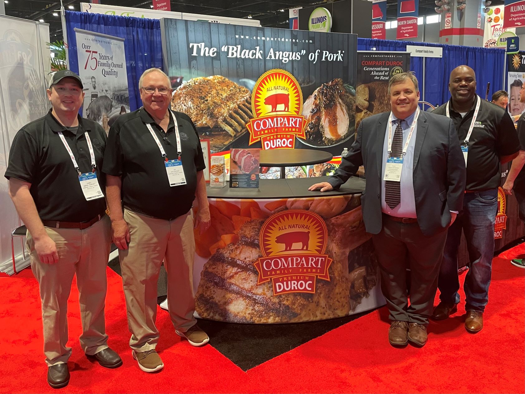 two men standing on each side of the Compart Duroc exhibit at a trade show