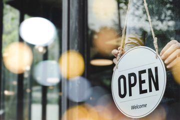 Business with person showing open sign on window.