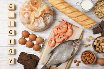 Collage of breads, eggs, seafood, and nuts with the word allergy vertically shown on the left of picture.