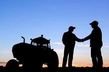 two farmers standing in field near tractor shaking hands