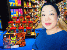 Smiling woman in blue in front of a display of packaged food in a grocery store